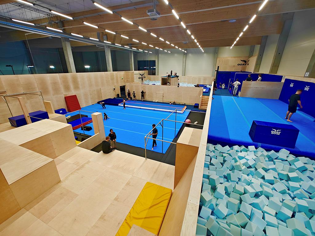 Sisäparkour-alue, jossa useita harjoittelevia henkilöitä sinisellä matolla. Vaneripintaiset seinät ja erilaisia harjoitusvälineitä.
